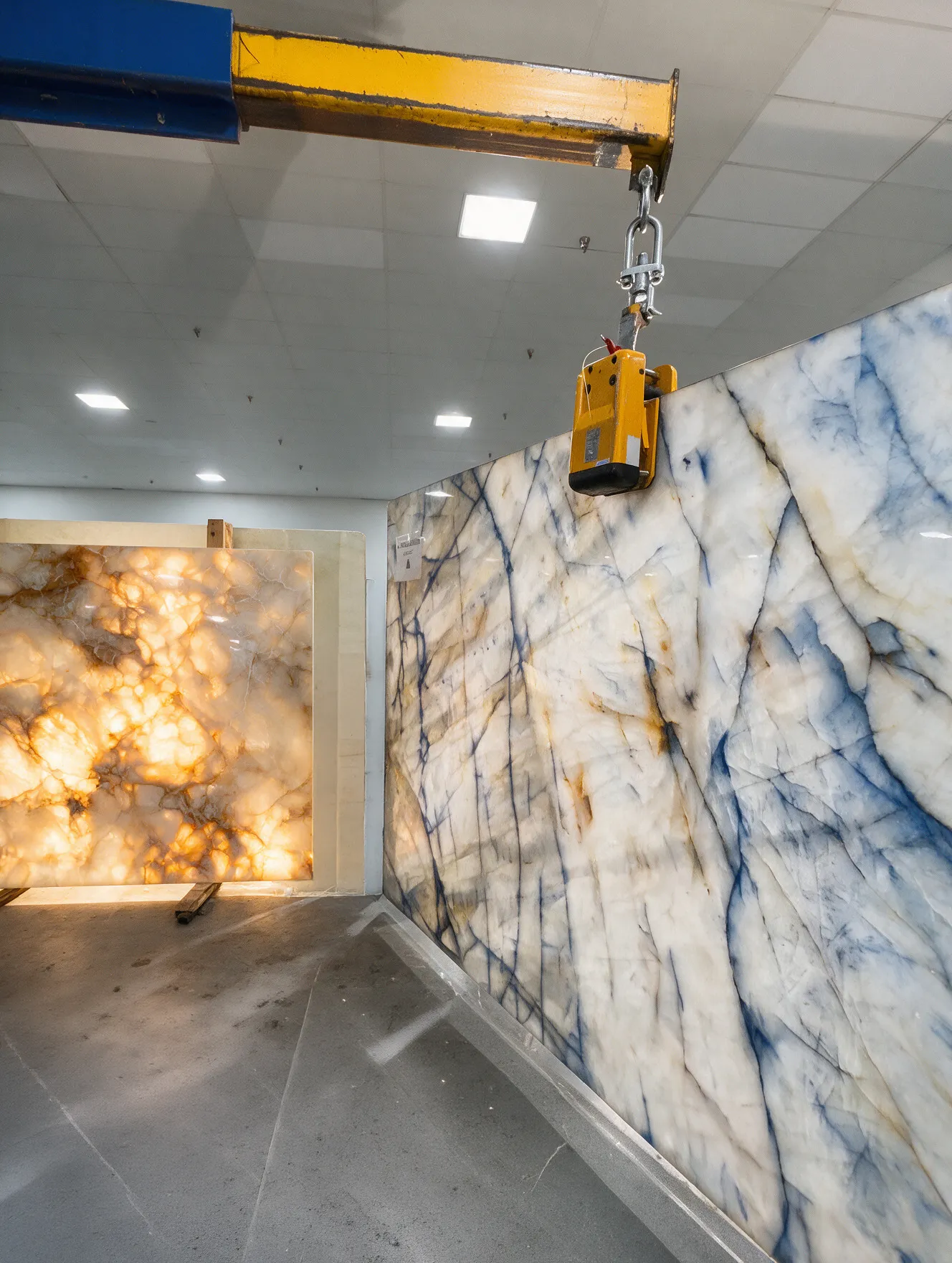 Blue quartzite slab being lifted next to a backlit onyx slab in the warehouse